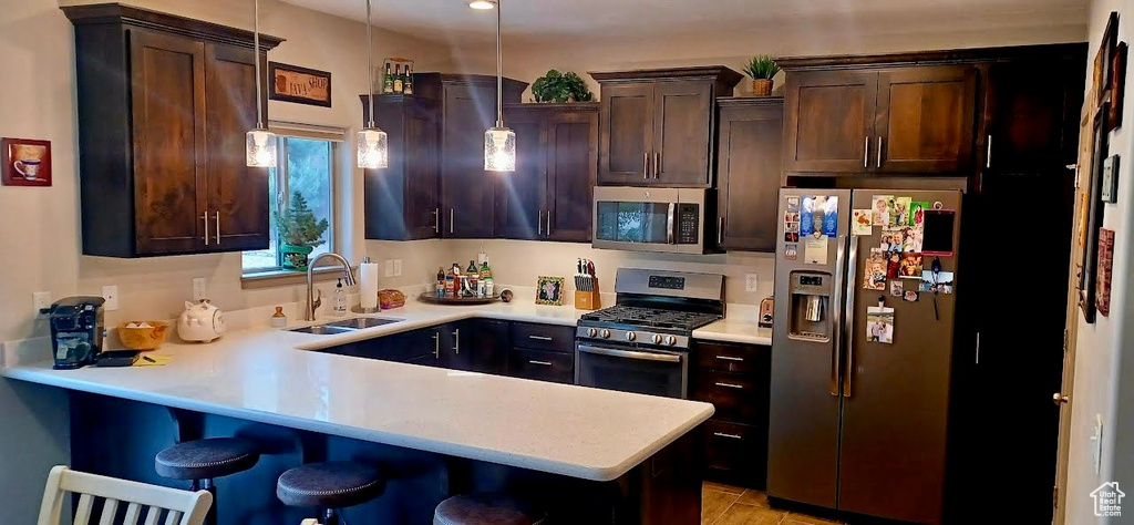 Kitchen with appliances with stainless steel finishes, a sink, dark brown cabinets, light countertops, and a peninsula