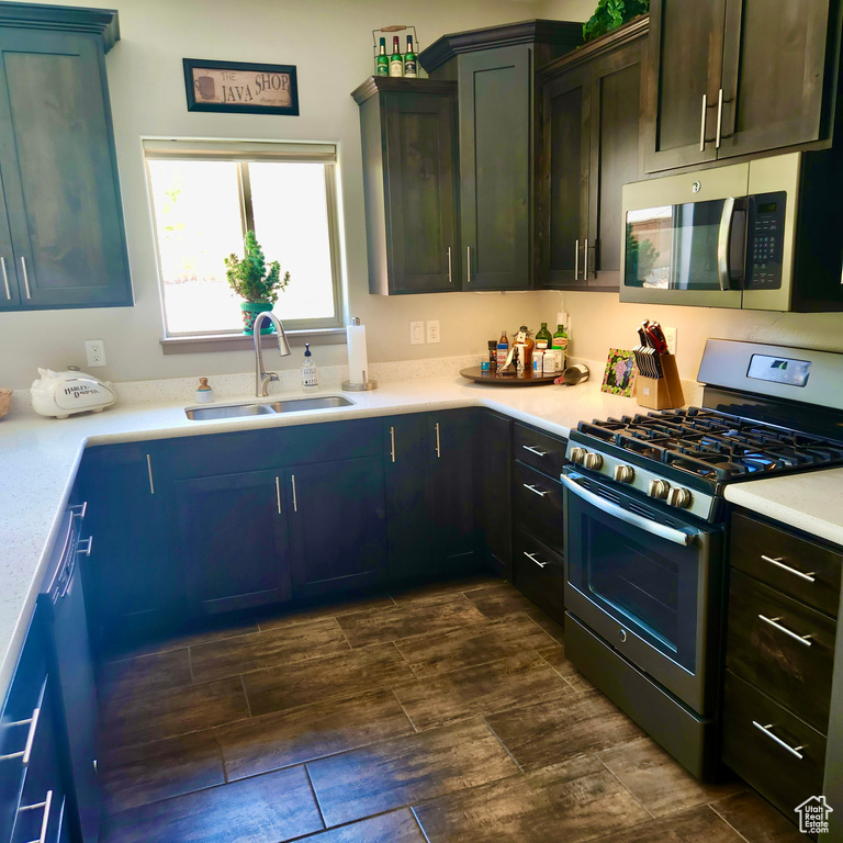 Kitchen featuring appliances with stainless steel finishes, a sink, wood tiled floors, and light countertops