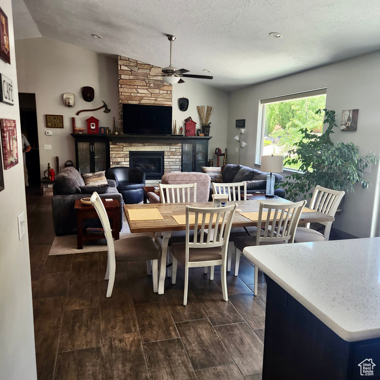 Dining area with ceiling fan, a stone fireplace, lofted ceiling, dark wood-type flooring, and a textured ceiling