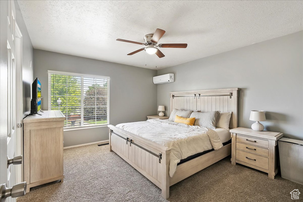 Carpeted bedroom featuring an AC wall unit, a textured ceiling, baseboards, and a ceiling fan