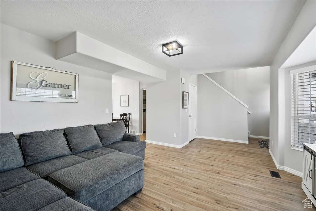 Living area featuring light wood-style floors, baseboards, a textured ceiling, and stairway
