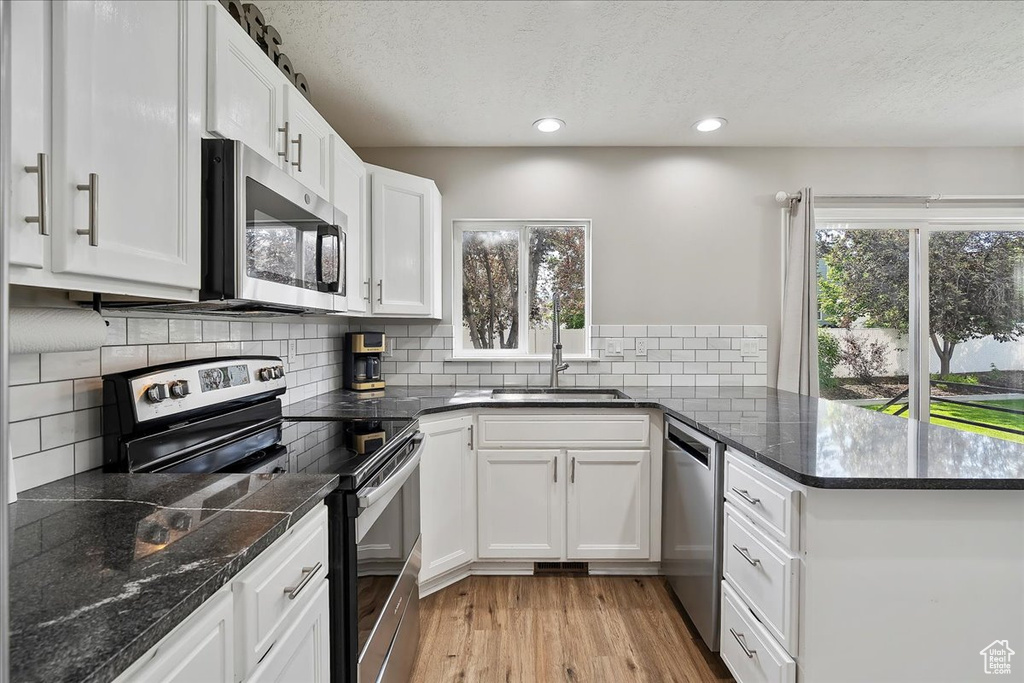 Kitchen featuring stainless steel appliances, a sink, a peninsula, a textured ceiling, and plenty of natural light