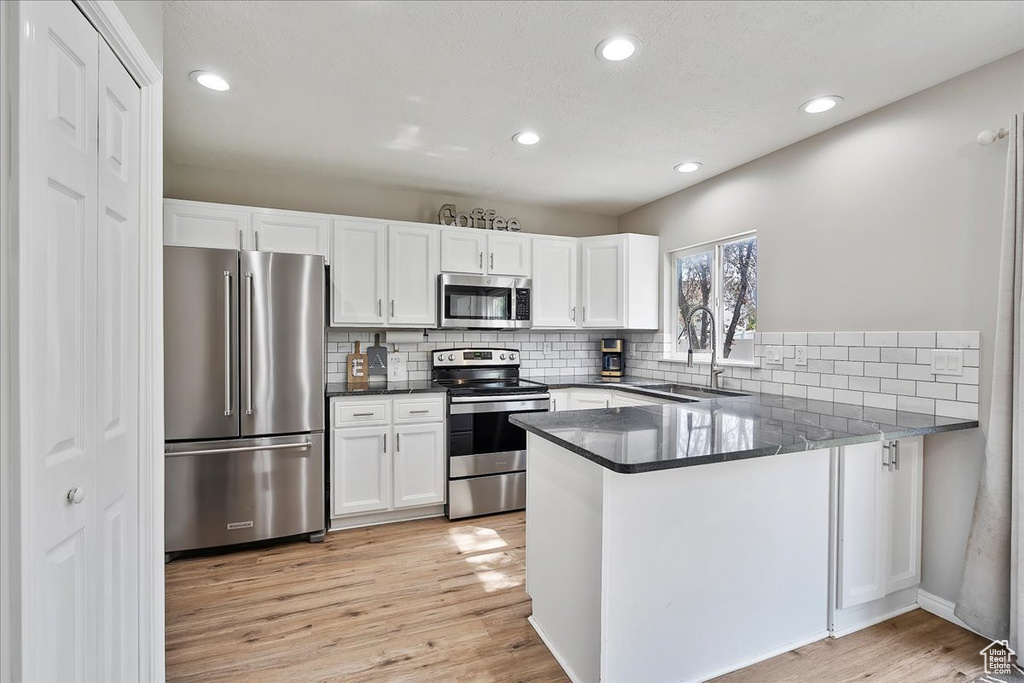 Kitchen featuring appliances with stainless steel finishes, a sink, white cabinets, tasteful backsplash, and recessed lighting