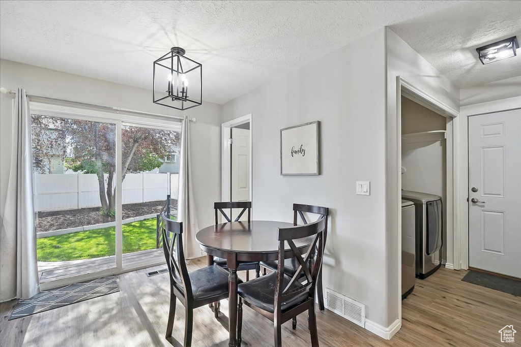Dining space featuring a chandelier, wood finished floors, baseboards, a textured ceiling, and washing machine and clothes dryer