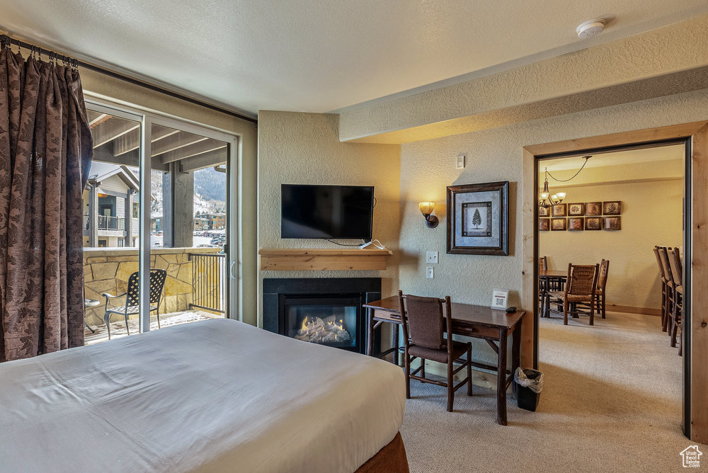 Bedroom featuring a textured wall, access to outside, a chandelier, carpet floors, and a glass covered fireplace