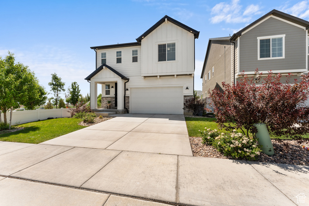 View of front of property featuring board and batten siding, an attached garage, concrete driveway, and stone siding
