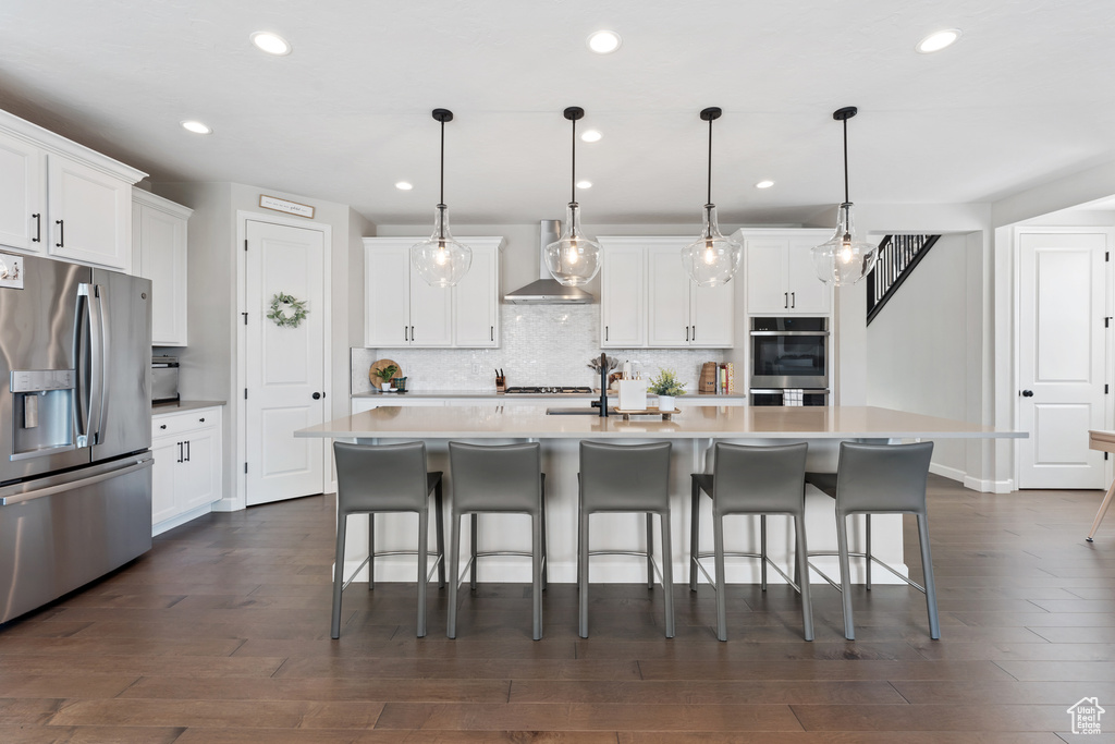 Kitchen with stainless steel appliances, wall chimney exhaust hood, recessed lighting, tasteful backsplash, and light countertops