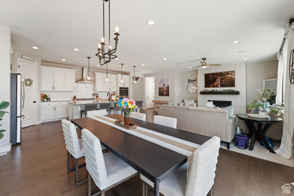 Dining room with a fireplace, dark wood-style floors, recessed lighting, ceiling fan, and a chandelier