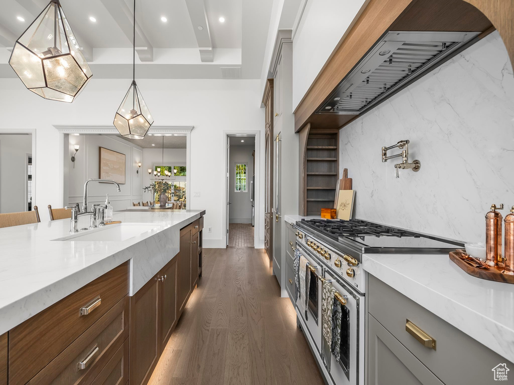 Kitchen featuring double oven range, a sink, dark wood finished floors, light stone counters, and decorative light fixtures