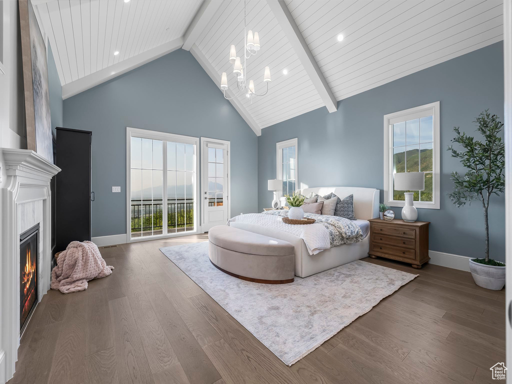 Bedroom featuring a chandelier, a glass covered fireplace, baseboards, wood finished floors, and high vaulted ceiling