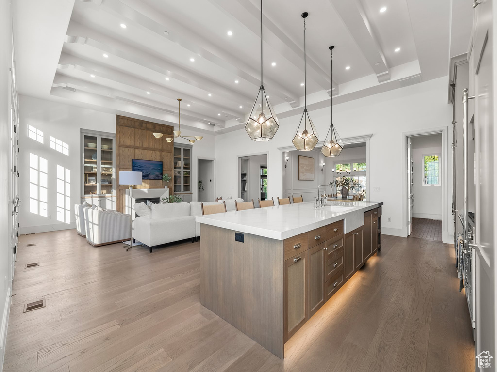 Kitchen with light countertops, a large island with sink, wood finished floors, pendant lighting, and recessed lighting