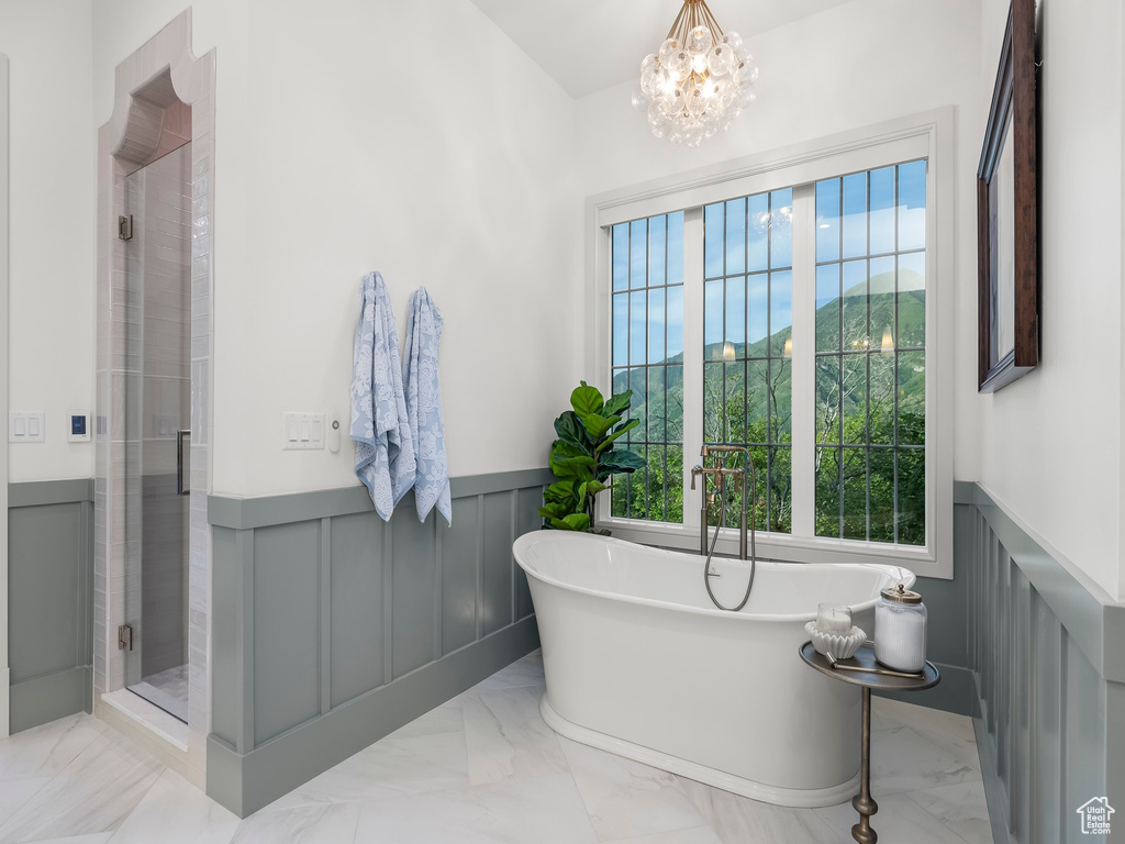 Bathroom featuring marble tiled flooring, a wainscoted wall, a stall shower, a freestanding tub, and a chandelier