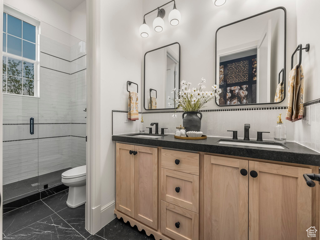 Bathroom featuring marble finish floors, toilet, a stall shower, and double vanity