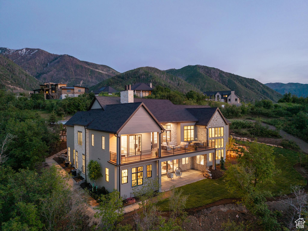 Back of house at dusk featuring a balcony, a mountain view, a patio area, and a chimney