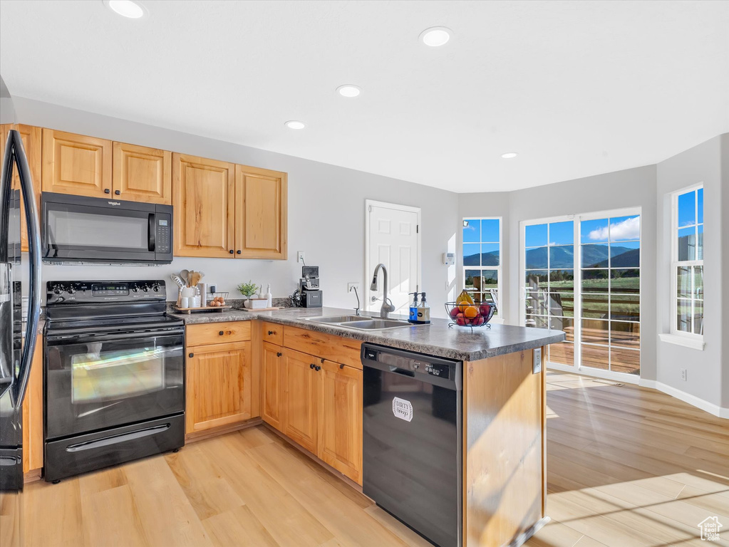 Kitchen featuring black appliances, a sink, a peninsula, light wood-style flooring, and recessed lighting