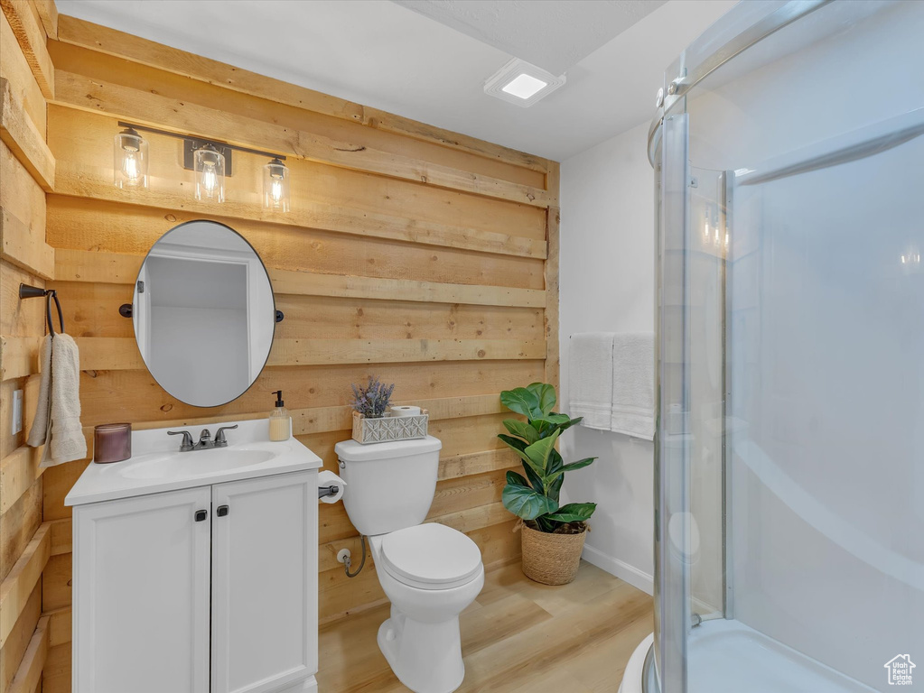 Bathroom featuring vanity, toilet, a stall shower, wooden walls, and wood finished floors
