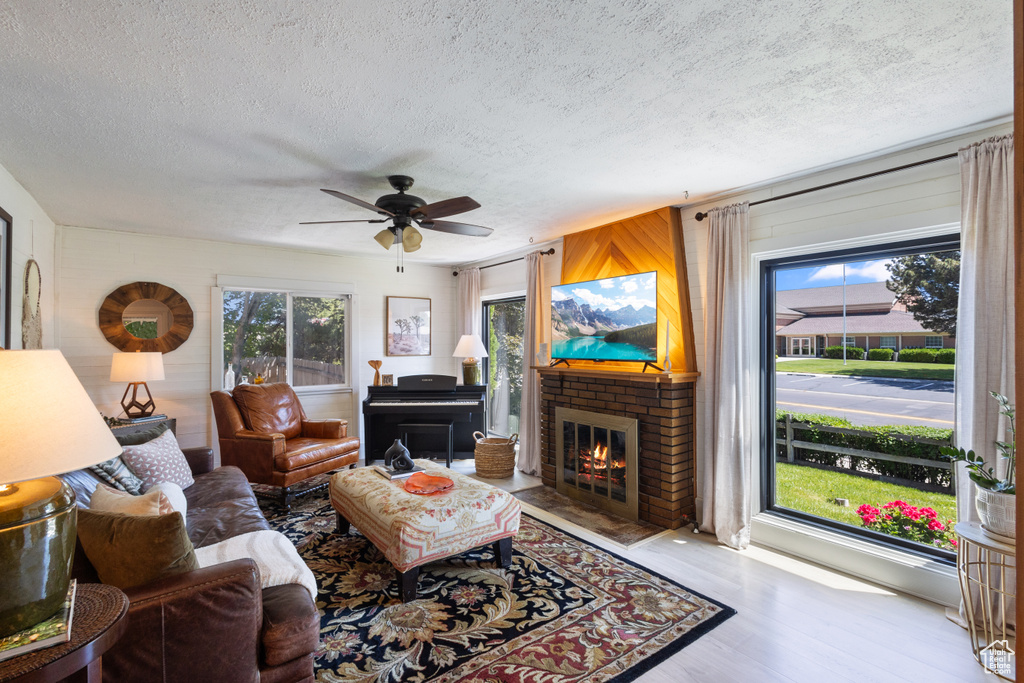 Living room with a fireplace, a textured ceiling, wood finished floors, healthy amount of natural light, and ceiling fan