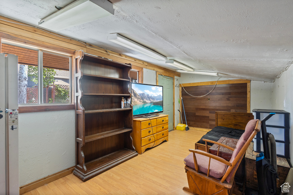 Below grade area featuring wooden walls, wood finished floors, freestanding refrigerator, and a textured ceiling