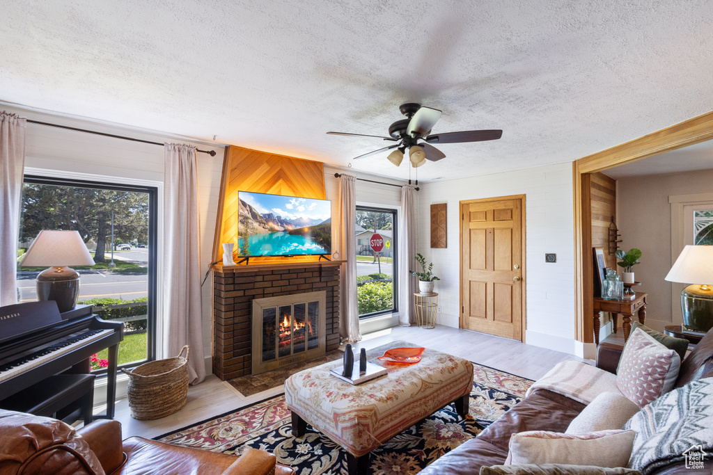 Living room featuring a textured ceiling, plenty of natural light, a fireplace, a ceiling fan, and light wood finished floors