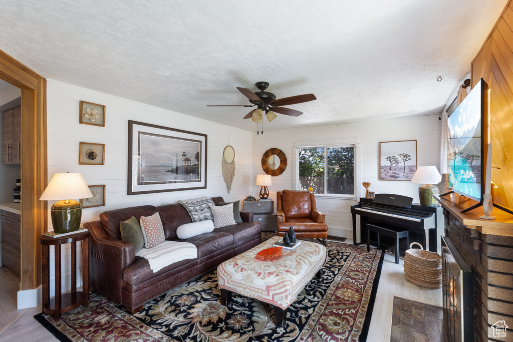 Living room with wood finished floors, ceiling fan, wood walls, and a textured ceiling