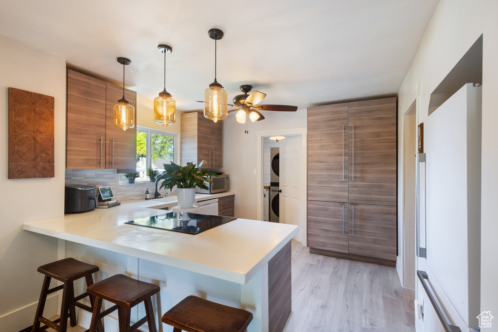 Kitchen with stacked washer / drying machine, brown cabinetry, black electric stovetop, a kitchen breakfast bar, and modern cabinets