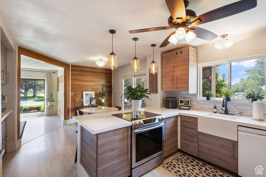 Kitchen with stainless steel range with electric stovetop, white dishwasher, a peninsula, light countertops, and wood walls