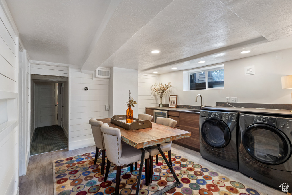 Dining room with a textured ceiling, light wood-style floors, washing machine and clothes dryer, recessed lighting, and wooden walls
