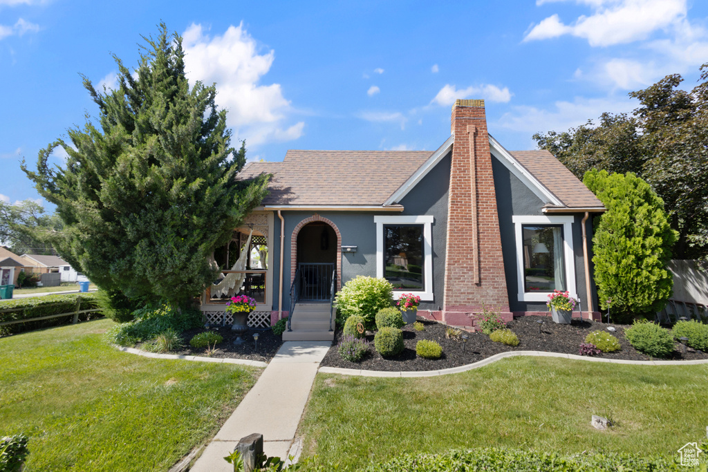 View of front facade with a porch, a front yard, a chimney, and stucco siding
