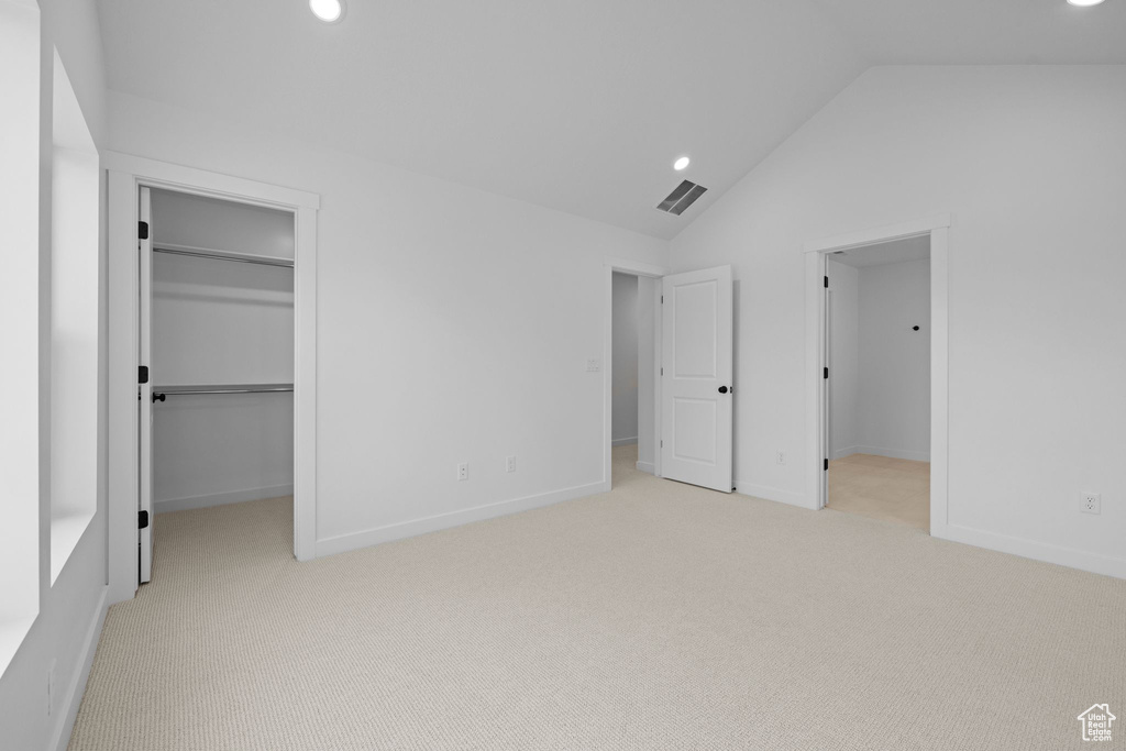 Unfurnished bedroom with a spacious closet, vaulted ceiling, light carpet, recessed lighting, and a closet