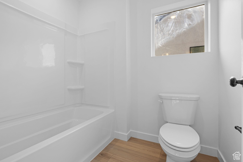 Bathroom with wood finished floors, baseboards, toilet, and shower / washtub combination