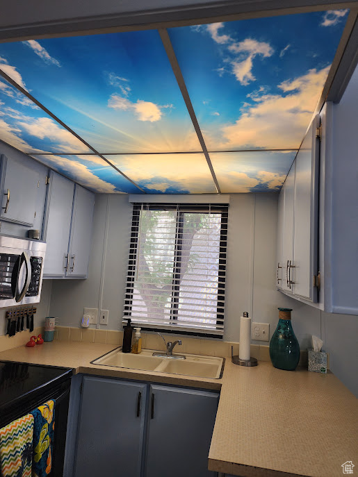 Kitchen with stainless steel microwave, a sink, light countertops, and black electric range oven