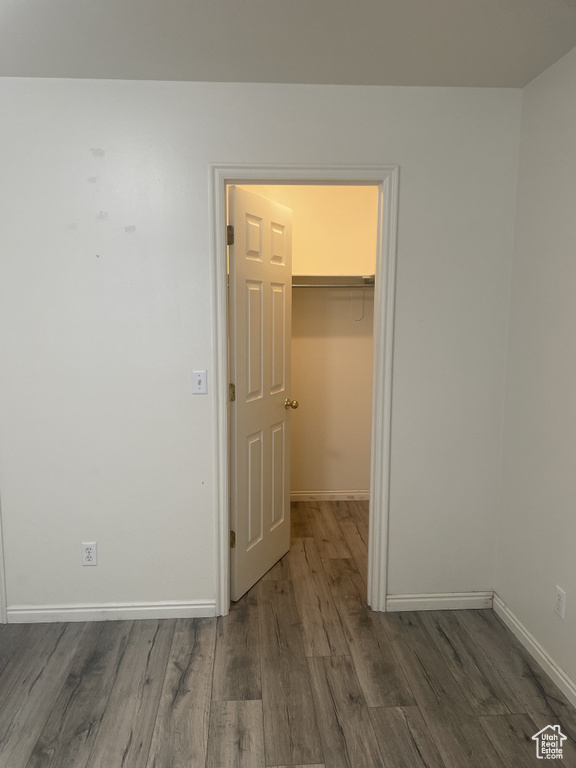 Unfurnished bedroom with wood finished floors, a spacious closet, baseboards, and a closet