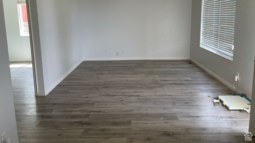 Empty room with dark wood finished floors, baseboards, and healthy amount of natural light