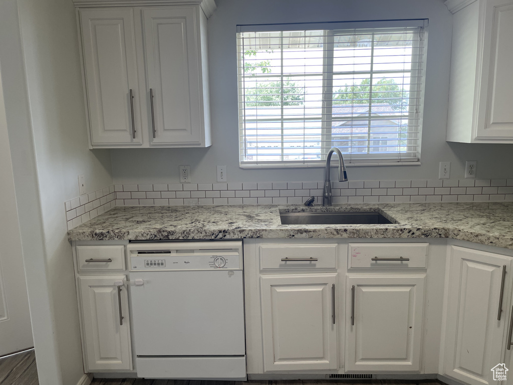 Kitchen with white dishwasher, a sink, white cabinetry, and healthy amount of natural light
