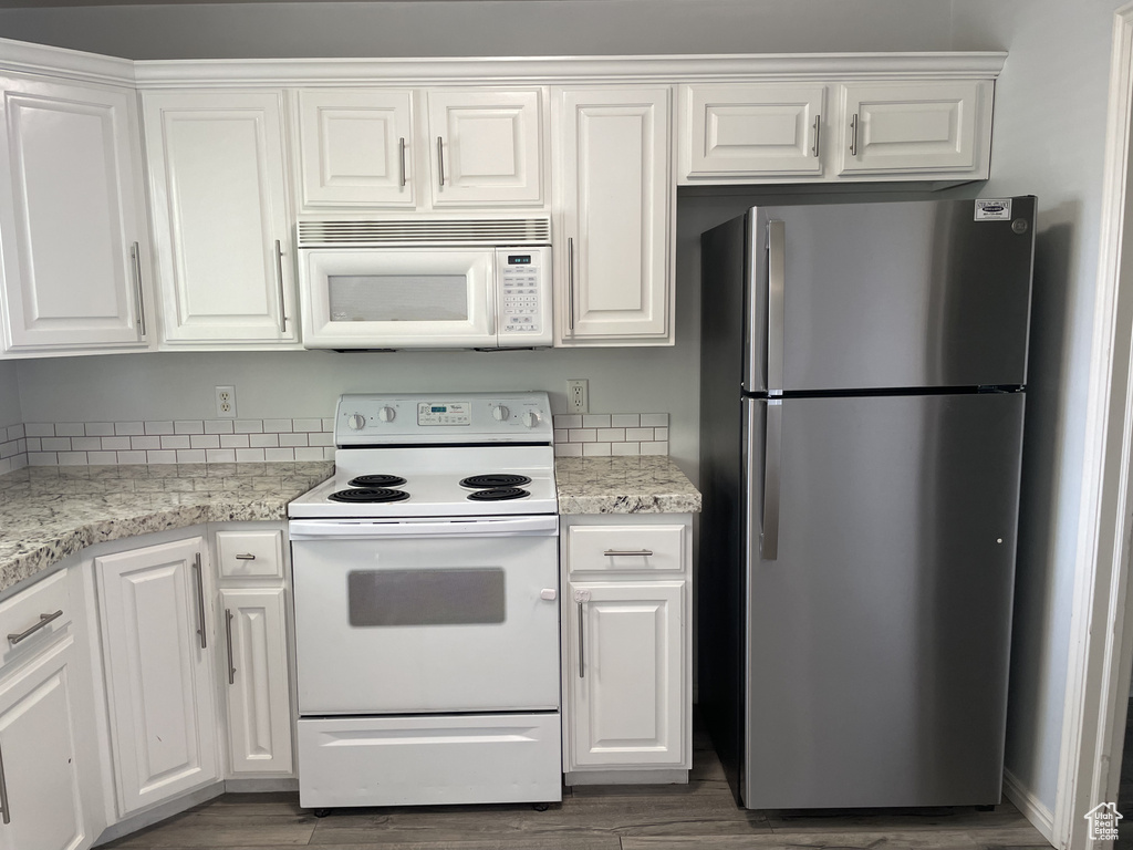 Kitchen with white appliances, white cabinets, and wood finished floors