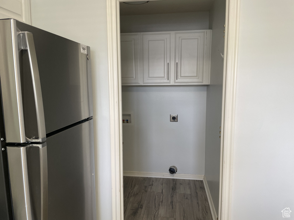 Laundry area with hookup for an electric dryer, hookup for a washing machine, cabinet space, wood finished floors, and baseboards