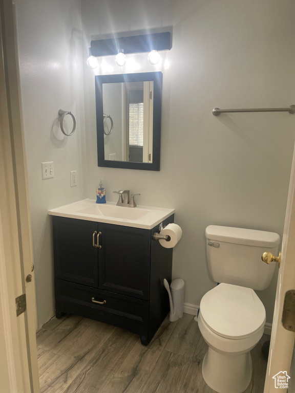 Half bathroom with vanity, wood finished floors, toilet, and baseboards
