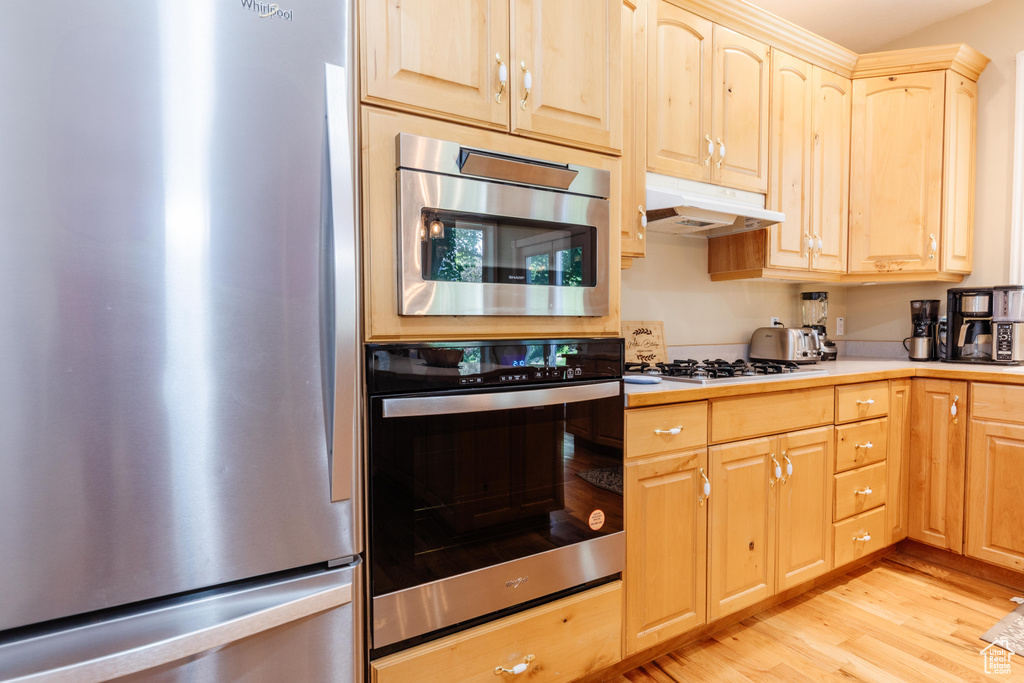 Kitchen with appliances with stainless steel finishes, under cabinet range hood, light brown cabinetry, and light wood-style flooring