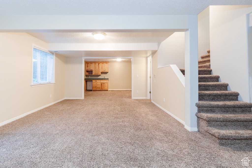 Unfurnished living room with light colored carpet, stairway, and baseboards