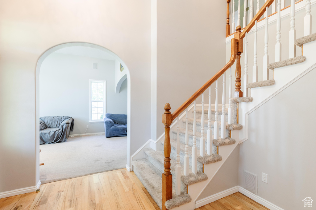 Stairway with arched walkways, wood finished floors, baseboards, a high ceiling, and carpet floors