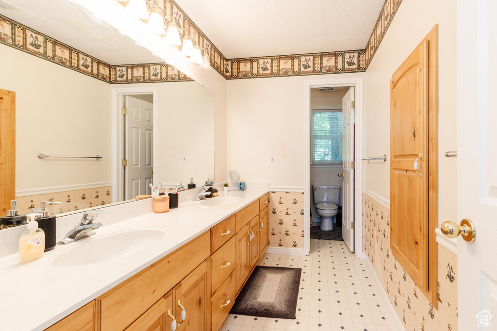 Bathroom with double vanity, tile patterned floors, toilet, and wainscoting