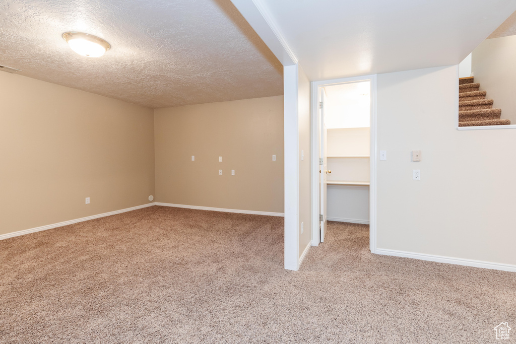 Below grade area with light carpet, stairway, baseboards, and a textured ceiling