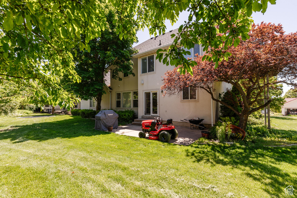 Rear view of property with a patio, a lawn, stucco siding, and a shingled roof