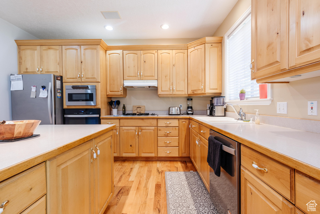 Kitchen with stainless steel appliances, light brown cabinets, a sink, under cabinet range hood, and light countertops