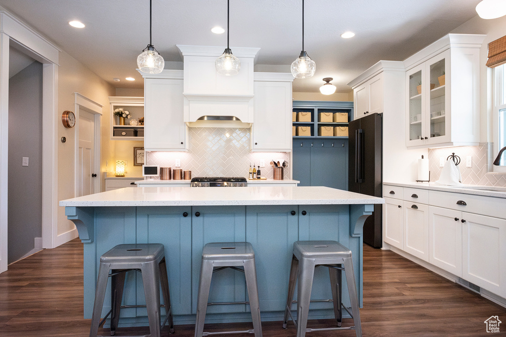 Kitchen with freestanding refrigerator, white cabinets, decorative backsplash, light countertops, and a kitchen island