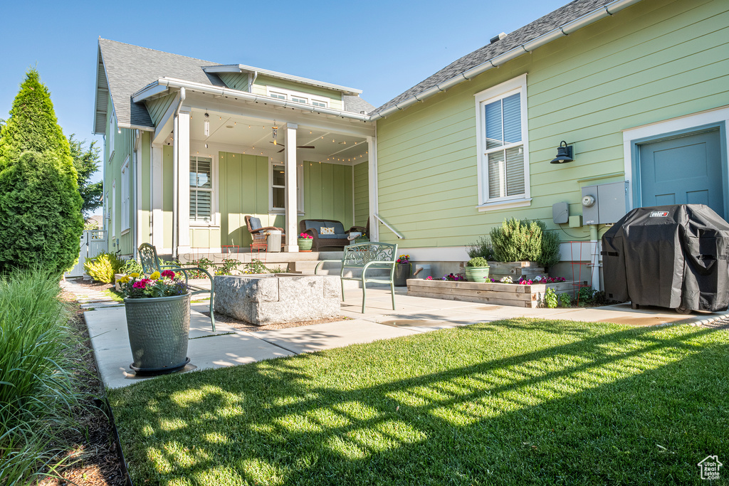 Back of house with a patio area, a lawn, a shingled roof, and board and batten siding