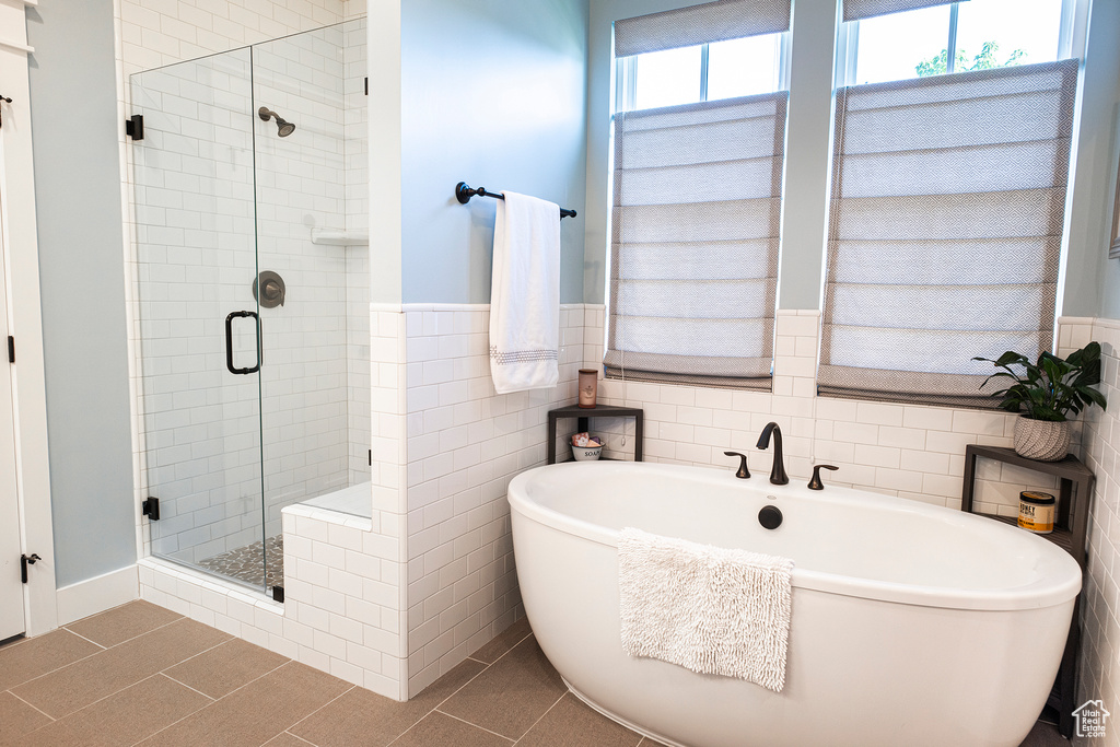 Bathroom featuring a freestanding tub, a shower stall, tile patterned flooring, tile walls, and a wainscoted wall