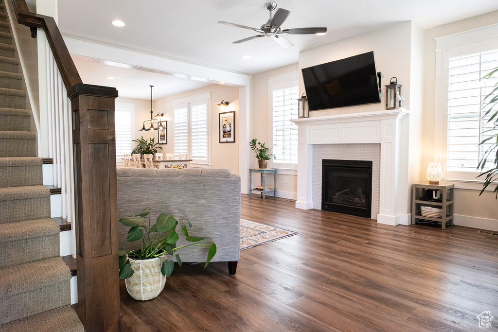 Living room with stairs, a ceiling fan, dark wood-style flooring, baseboards, and a tile fireplace