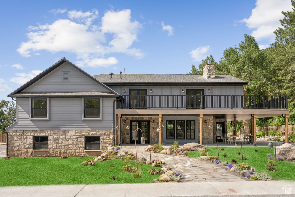 Rear view of property with french doors, a patio area, a chimney, stone siding, and a balcony