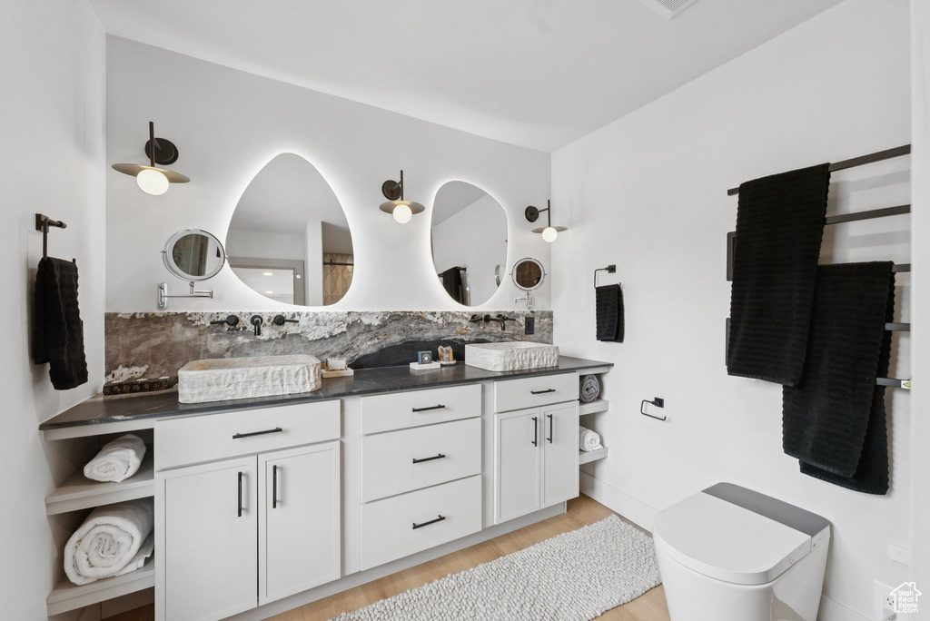 Full bath with double vanity, wood finished floors, and decorative backsplash